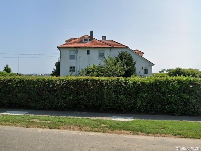 20 Brightwood St, Patchogue, NY 11772 - view of property exterior with a chimney, a tiled roof, and stucco siding