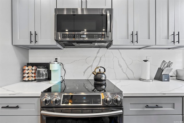 kitchen featuring backsplash, gray cabinets, light stone counters, and appliances with stainless steel finishes