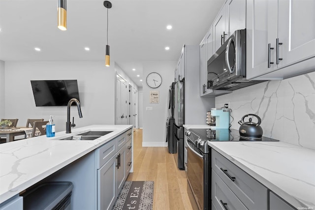 kitchen featuring light stone countertops, sink, pendant lighting, light hardwood / wood-style floors, and appliances with stainless steel finishes