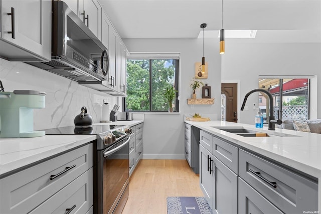 kitchen featuring appliances with stainless steel finishes, light wood-type flooring, light stone counters, sink, and pendant lighting