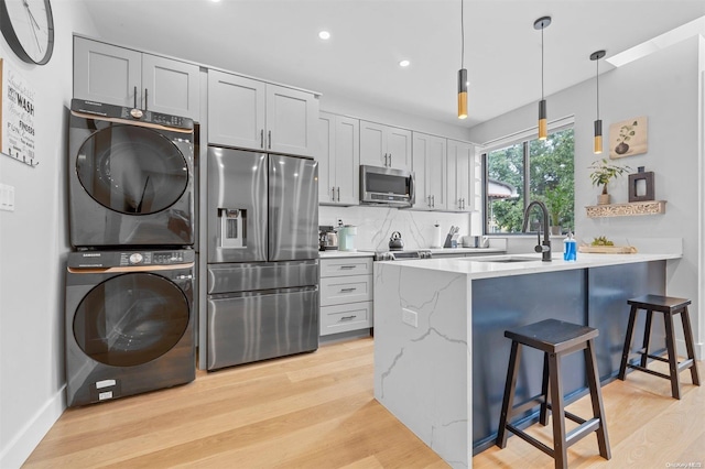 kitchen featuring a breakfast bar area, light hardwood / wood-style flooring, stacked washer and clothes dryer, and appliances with stainless steel finishes