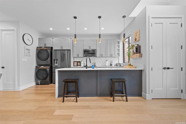 kitchen featuring pendant lighting, a kitchen breakfast bar, light wood-type flooring, stacked washer / drying machine, and stainless steel appliances