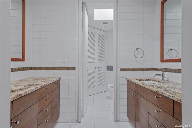 bathroom featuring tile patterned floors, vanity, toilet, and tile walls