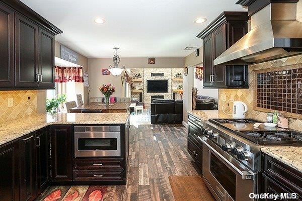 kitchen with wall chimney range hood, dark hardwood / wood-style floors, tasteful backsplash, decorative light fixtures, and stainless steel appliances