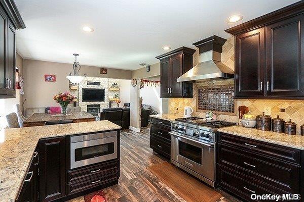 kitchen featuring light stone counters, dark hardwood / wood-style flooring, wall chimney exhaust hood, and stainless steel appliances