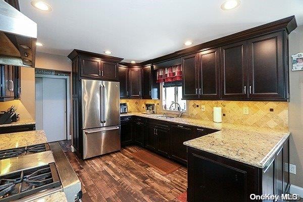 kitchen with sink, decorative backsplash, stainless steel fridge, light stone countertops, and dark hardwood / wood-style flooring