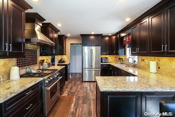 kitchen featuring wall chimney range hood, sink, dark hardwood / wood-style floors, light stone countertops, and appliances with stainless steel finishes