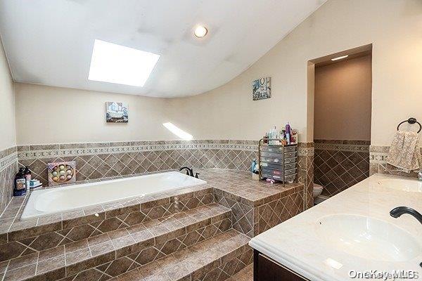 bathroom featuring vanity, a relaxing tiled tub, and vaulted ceiling with skylight