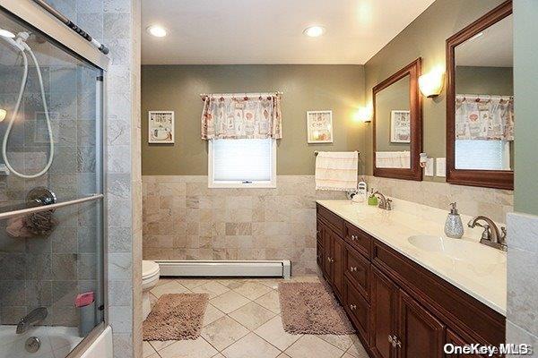 full bathroom featuring vanity, shower / bath combination with glass door, tile patterned flooring, tile walls, and a baseboard radiator