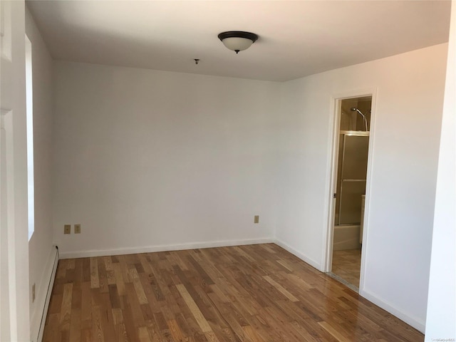 unfurnished bedroom with a walk in closet, a closet, hardwood / wood-style floors, and a baseboard radiator