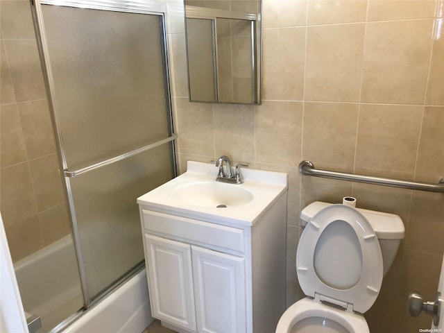 full bathroom featuring vanity, toilet, shower / bath combination with glass door, and tile walls