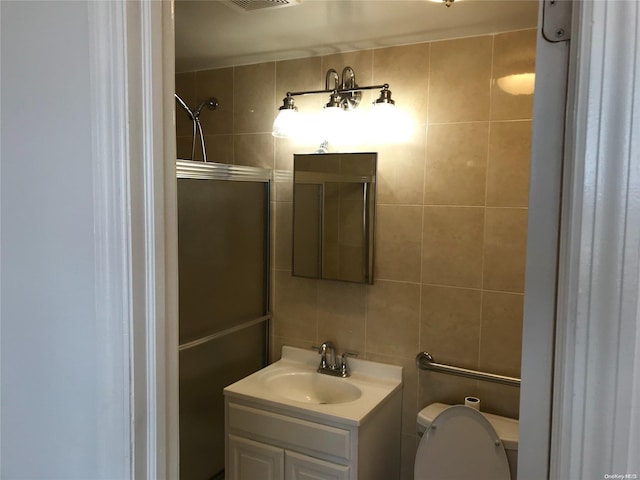 bathroom featuring backsplash, toilet, vanity, a shower with shower door, and tile walls