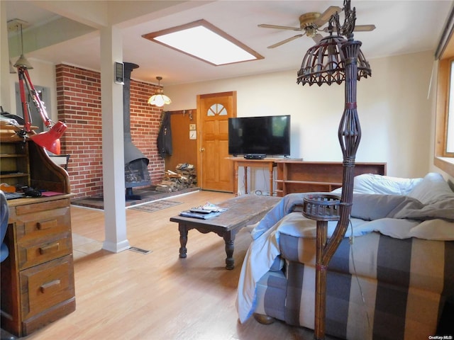 living room with a wood stove, ceiling fan, brick wall, and light wood-type flooring