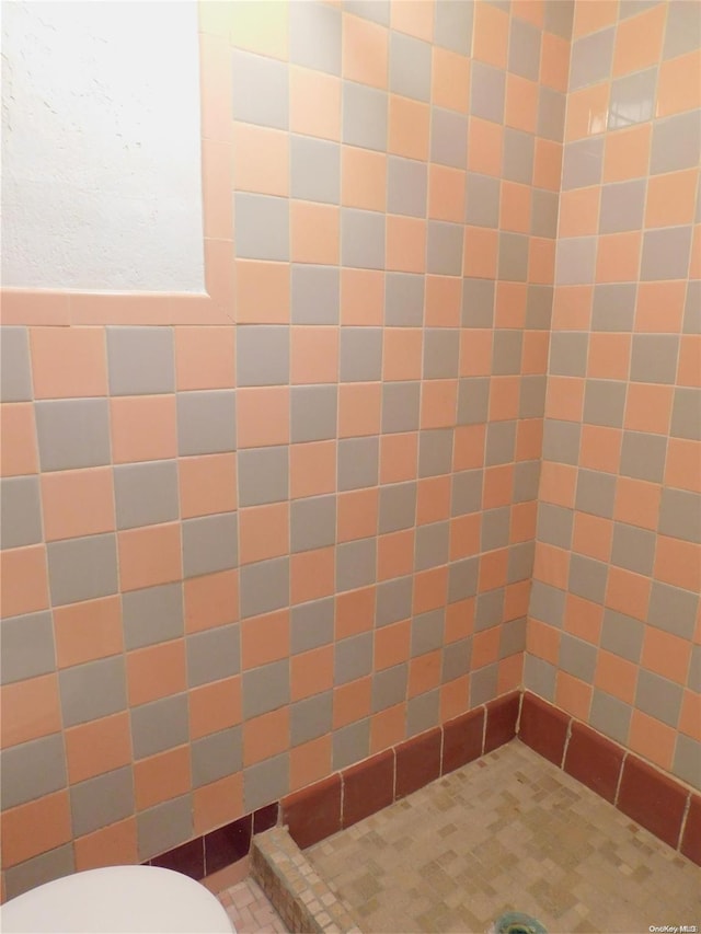 bathroom with toilet, tile walls, and a tile shower