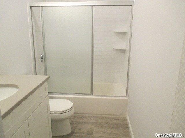 full bathroom featuring enclosed tub / shower combo, toilet, wood-type flooring, and vanity