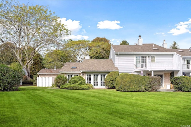 back of property with french doors, a balcony, and a lawn