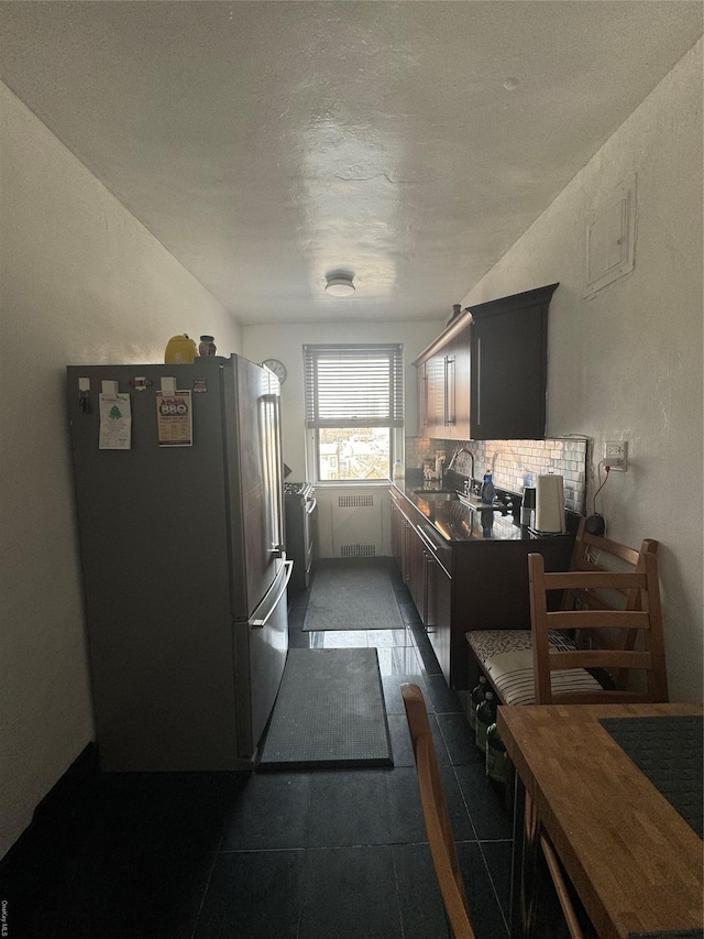 kitchen featuring radiator, sink, stainless steel fridge, tasteful backsplash, and dark tile patterned flooring