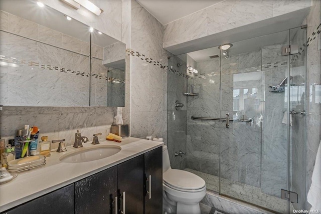 bathroom with a shower with door, vanity, tile walls, and toilet