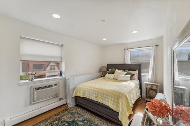 bedroom with baseboard heating, wood-type flooring, and an AC wall unit