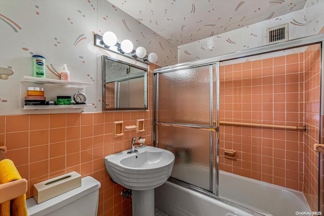 bathroom with toilet, shower / bath combination with glass door, and tile walls