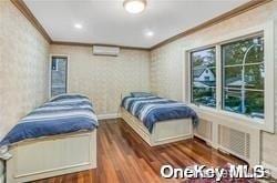 bedroom featuring ornamental molding, a wall unit AC, and dark wood-type flooring