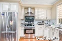 kitchen featuring white cabinets, sink, stainless steel appliances, and wall chimney range hood