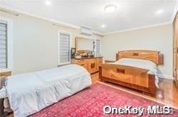 bedroom featuring a wall mounted air conditioner, hardwood / wood-style flooring, and ornamental molding