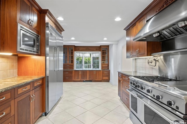 kitchen featuring tasteful backsplash, built in appliances, stone counters, and exhaust hood