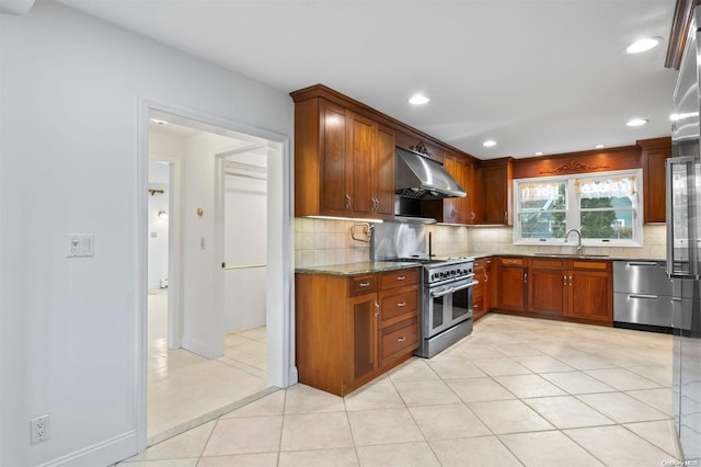 kitchen with appliances with stainless steel finishes, sink, wall chimney range hood, light tile patterned floors, and stone counters