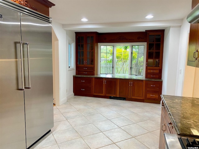 kitchen with light tile patterned floors, stainless steel built in refrigerator, and dark stone counters