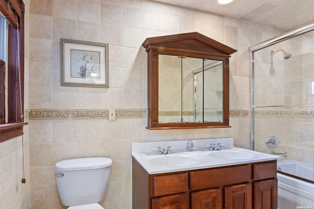 full bathroom with combined bath / shower with glass door, vanity, toilet, and tile walls