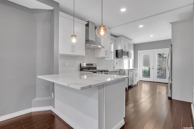 kitchen featuring white cabinets, wall chimney exhaust hood, hanging light fixtures, and appliances with stainless steel finishes