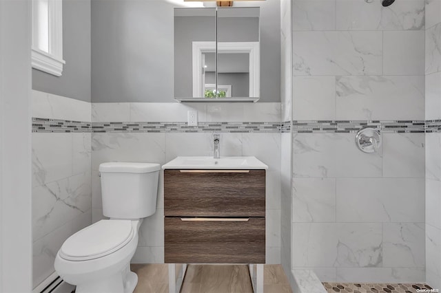 bathroom with a tile shower, vanity, baseboard heating, and tile walls