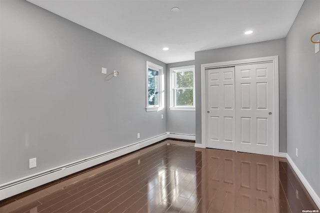 unfurnished bedroom featuring dark wood-type flooring, a closet, and a baseboard heating unit