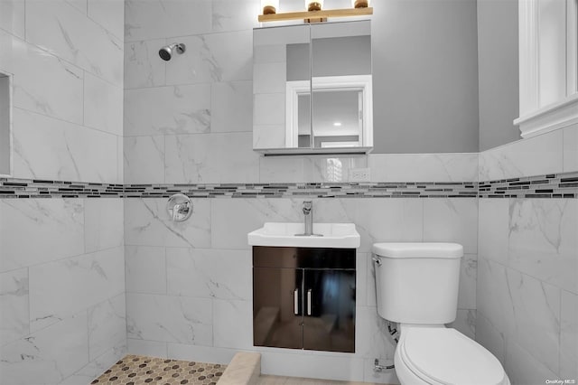 bathroom with vanity, toilet, tiled shower, and tile walls