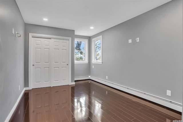 unfurnished bedroom with hardwood / wood-style floors, a baseboard radiator, and a closet