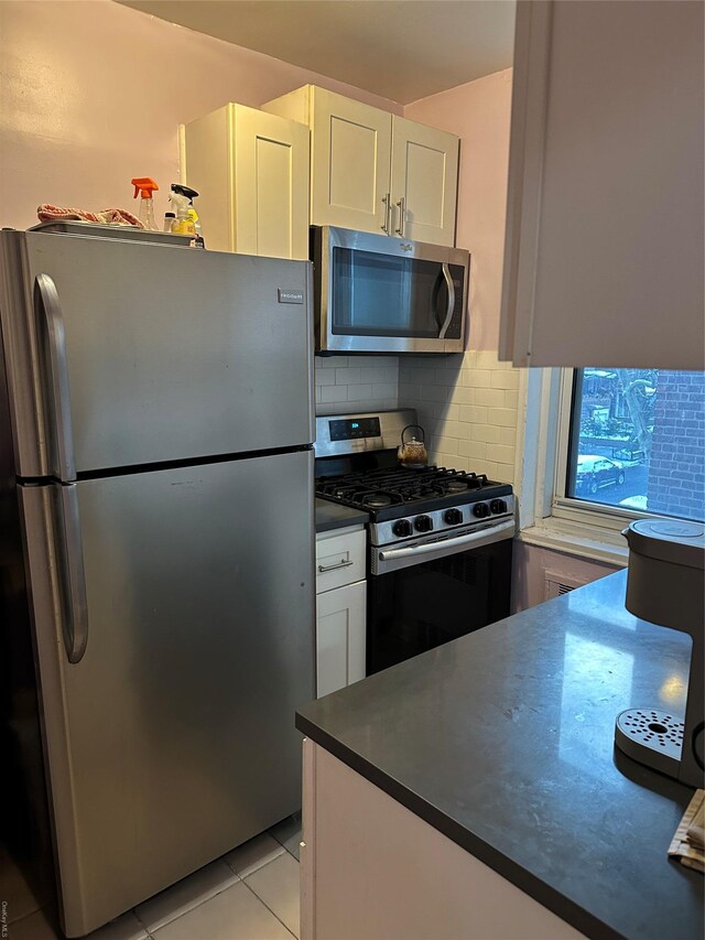 kitchen with appliances with stainless steel finishes, light tile patterned floors, tasteful backsplash, and white cabinetry