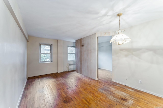 spare room featuring hardwood / wood-style floors, radiator, and a notable chandelier