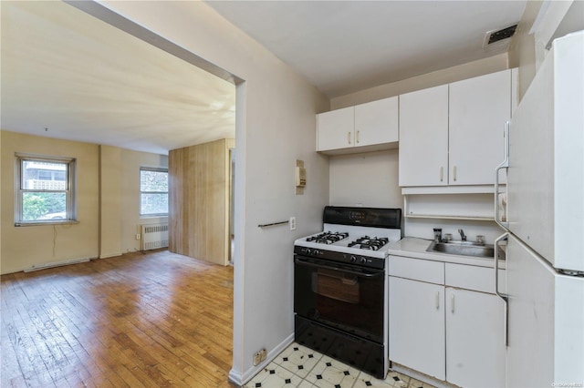 kitchen with gas stove, white refrigerator, light hardwood / wood-style flooring, white cabinets, and radiator heating unit