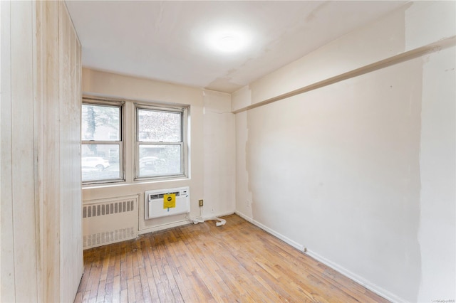 unfurnished room featuring radiator heating unit, light wood-type flooring, and a wall unit AC