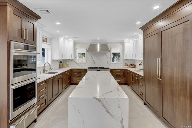 kitchen with light stone countertops, tasteful backsplash, stainless steel appliances, sink, and wall chimney range hood