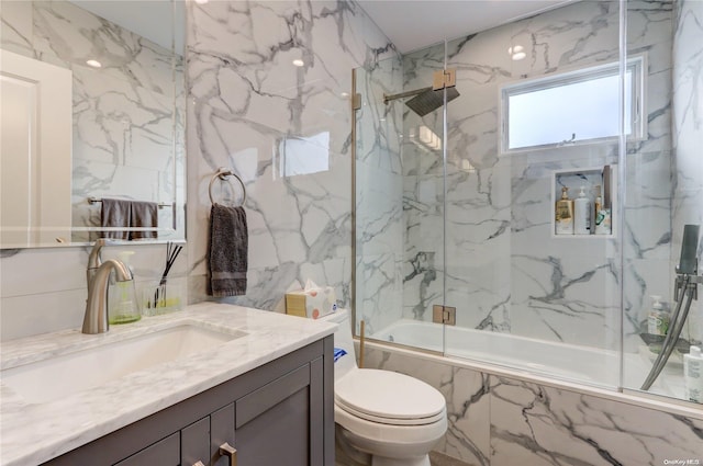 full bathroom featuring shower / bath combination with glass door, vanity, toilet, and tile walls