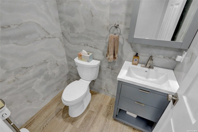 bathroom featuring vanity, toilet, wood-type flooring, and tile walls