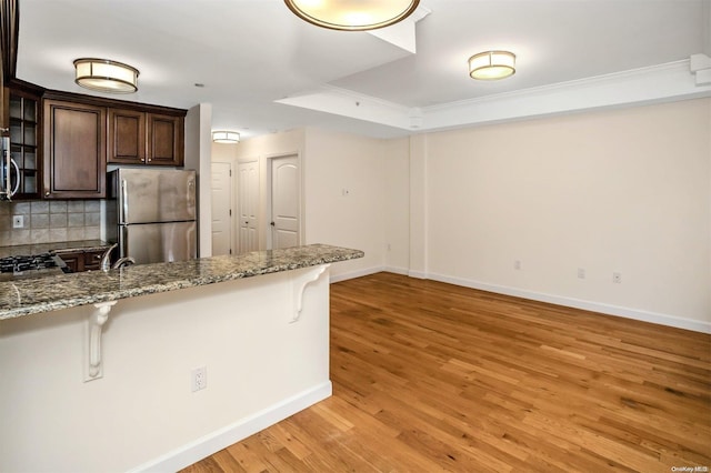 kitchen with light stone counters, light hardwood / wood-style flooring, backsplash, a breakfast bar area, and appliances with stainless steel finishes