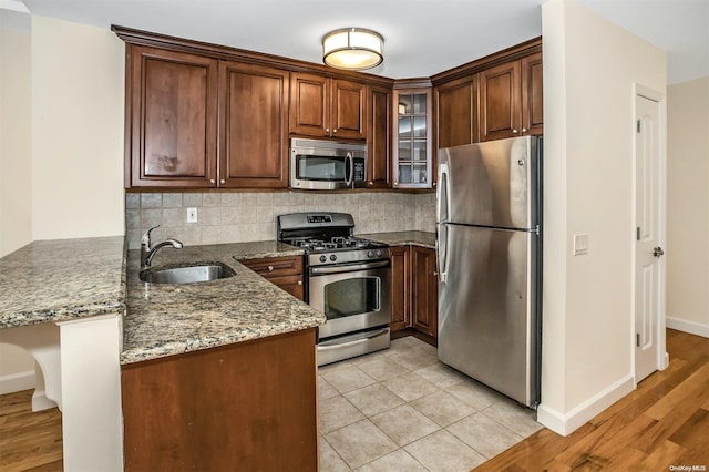 kitchen with stone counters, light hardwood / wood-style flooring, backsplash, kitchen peninsula, and appliances with stainless steel finishes