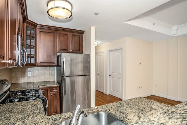 kitchen with backsplash, light stone counters, stainless steel appliances, and light hardwood / wood-style floors