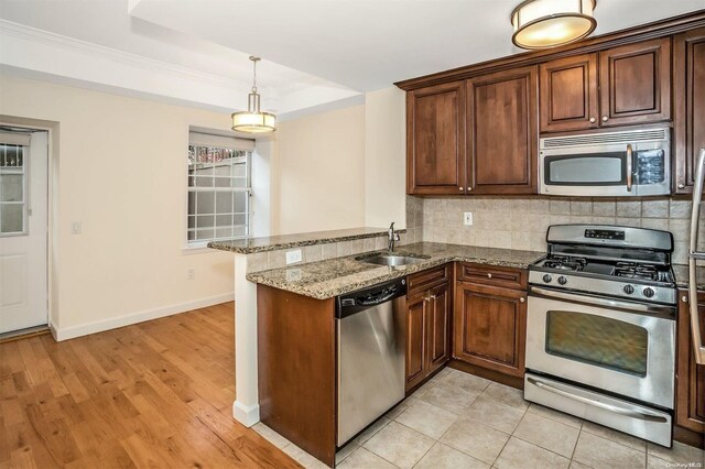 kitchen with sink, appliances with stainless steel finishes, light hardwood / wood-style floors, light stone counters, and kitchen peninsula