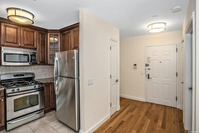 kitchen featuring decorative backsplash, light wood-type flooring, dark brown cabinets, stainless steel appliances, and dark stone countertops