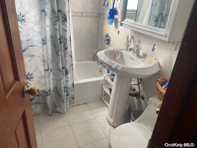 full bathroom featuring tasteful backsplash, tile patterned flooring, toilet, shower / bath combo with shower curtain, and tile walls