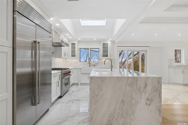 kitchen featuring light stone countertops, a skylight, high end appliances, sink, and white cabinets